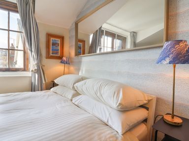 A bedroom with a bed white pillows a blue lamp two windows and a large mirror on the wall at Old Monmouth Lyme Regis