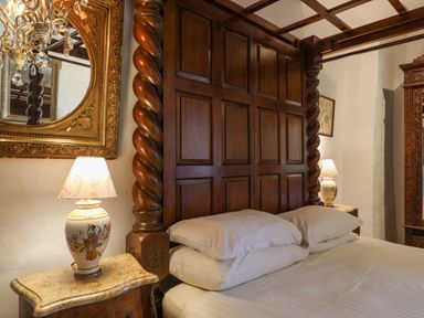 A bedroom with a wooden carved bed frame two bedside tables with lamps and a large ornate mirror at Old Monmouth in Lyme Regis