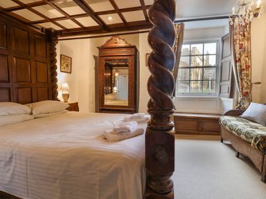 A bedroom with a four-poster bed white pillows a wooden mirror and a couch near a window at Old Monmouth in Lyme Regis