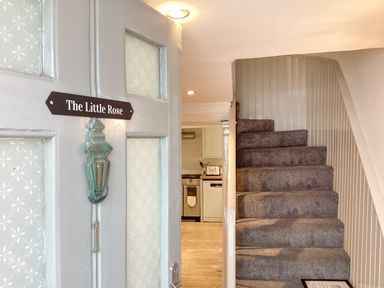 An open door with a sign The Little Rose showing a carpeted staircase and a kitchen in the background at The Little Rose in Lyme Regis