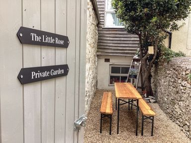 A private garden with a wooden table and benches next to stone walls and a tree at The Little Rose in Lyme Regis
