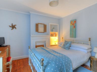 A bedroom with a white metal bed blue polka dot blanket a wooden desk with a TV and a bookshelf with a lamp at Driftwood Lyme Regis