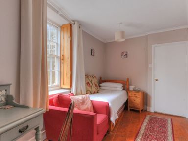 A bedroom with a wooden bed beside a window and a red armchair near a desk at Driftwood in Lyme Regis