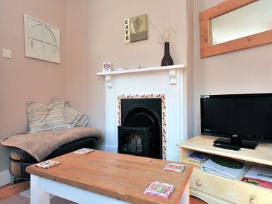 A living room with a fireplace a TV on a stand a wooden coffee table and a cushioned chair at Driftwood in Lyme Regis