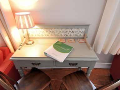 A desk with a table lamp a brochure and two wooden chairs at Driftwood in Lyme Regis