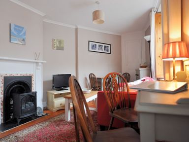 A living room with wooden chairs a red sofa a small fireplace a television and framed pictures on the wall at Driftwood in Lyme Regis