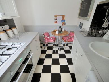 A kitchen with a checkered black and white floor a small round table with two chairs and kitchen appliances at Driftwood Lyme Regis