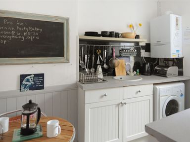 A kitchen with a sink utensils hanging above counter and a washing machine below counter at Driftwood in Lyme Regis