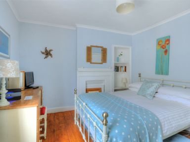 A bedroom with a bed blue blanket a wooden dresser a lamp a small TV and a built in bookshelf at Driftwood in Lyme Regis