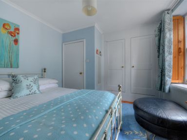 A bedroom with a bed with blue polka dot blanket a black ottoman and two white doors at Driftwood in Lyme Regis