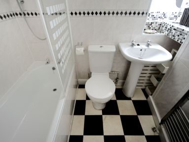 A bathroom with a bathtub shower toilet sink and black and white checkered floor at Driftwood in Lyme Regis