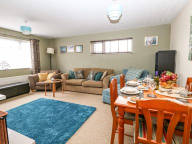 A living room with sofas a blue rug a dining table set with dishes and fruit bowl at Sunny Haven in Preston