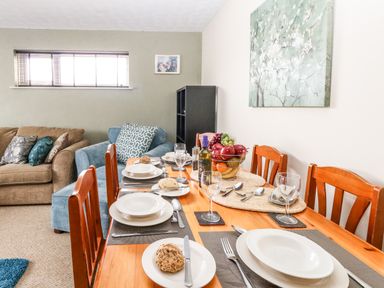 A dining table set with plates wine glasses cutlery and a fruit basket in a room with sofas and a window at Sunny Haven in Preston