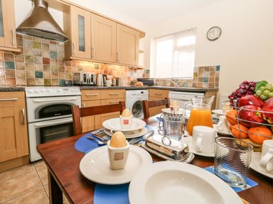 A kitchen with wooden cabinets a stove and a dining table set with plates eggs a jug of orange juice and a fruit basket at Sunny Haven in Preston