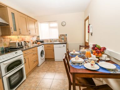 A kitchen with wooden cabinets a dining table set for four with fruit bowl and breakfast items at Sunny Haven in Preston