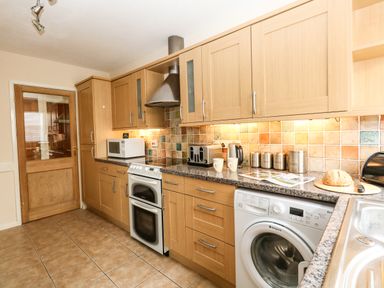 A kitchen with wooden cabinets a washing machine an oven microwave toaster kettle and bread on the counter at Sunny Haven in Preston