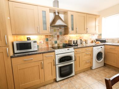 A kitchen with wooden cabinets microwave oven stove washing machine and toaster at Sunny Haven in Preston