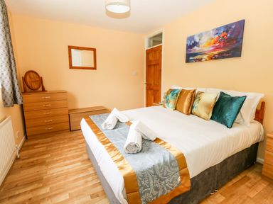 A bedroom with a double bed, multiple pillows, a dresser with a mirror, a wooden door, and a painting on the wall at Sunny Haven in Preston