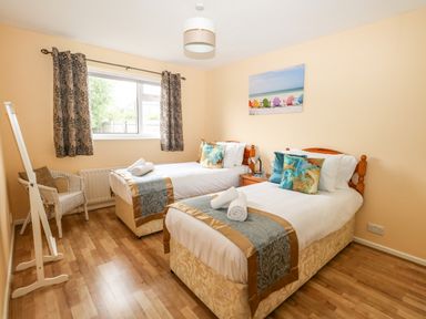A bedroom with two single beds with pillows and towels by a window with patterned curtains at Sunny Haven in Preston