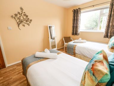 A bedroom with two single beds near a window with curtains a standing mirror and a chair at Sunny Haven in Preston