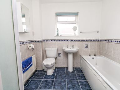 A bathroom with toilet sink and bathtub with blue tiled floor and white walls at Sunny Haven in Preston