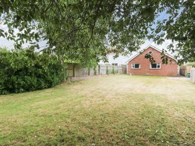A backyard with a lawn trees fence and a brick house at Sunny Haven in Preston