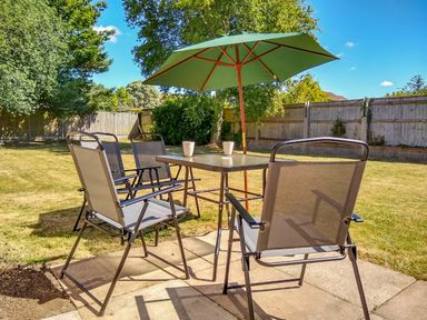An outdoor patio with four chairs around a table with a green umbrella in a fenced backyard at Sunny Haven in Preston