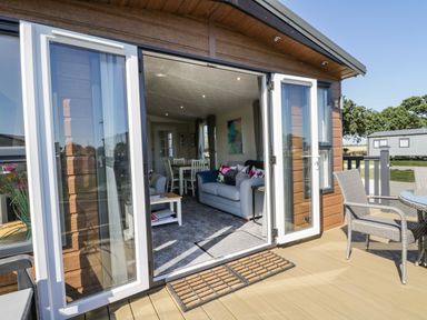 A deck with outdoor chairs and table looking into a living room with sofa and dining table at Away Daze in Carnaby near Bridlington