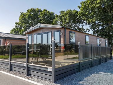 A modern caravan with glass and metal railing on a deck surrounded by trees at Away Daze in Carnaby near Bridlington