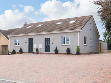 A brick paved driveway in front of a two door gray house with skylights and potted plants at Sawtons Cottage 2 in Dawlish