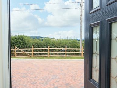 View through an open door showing a paved driveway a wooden fence green bushes and hills in the distance at Sawtons Cottage 2 in Dawlish