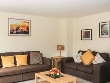 A living room with two brown sofas yellow and patterned cushions a wooden coffee table with flowers and framed pictures on the walls at Sawtons Cottage 2 in Dawlish