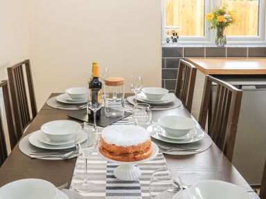 A dining table set with plates bowls glasses cutlery a cake in a kitchen at Sawtons Cottage 2 in Dawlish