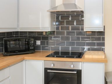 A kitchen corner with a black microwave oven wooden countertop electric stove stainless steel oven and white cabinets at Sawtons Cottage 2 in Dawlish