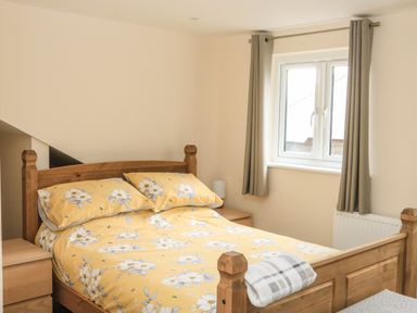 A bedroom with a wooden double bed with yellow floral bedding and gray curtains at Sawtons Cottage 2 in Dawlish