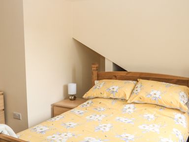 A bedroom with a wooden bed with yellow floral bedding and a wooden bedside table with a lamp at Sawtons Cottage 2 in Dawlish