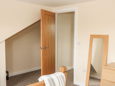 A bedroom corner with a wooden door open and a standing mirror next to a wooden chest of drawers at Sawtons Cottage 2 in Dawlish