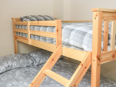 A wooden bunk bed with gray patterned bedding on the bottom and gray checkered bedding on the top at Sawtons Cottage 2 in Dawlish