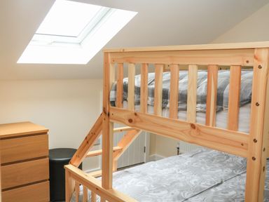 A bedroom with wooden bunk beds a chest of drawers a black stool and a skylight window at Sawtons Cottage 2 in Dawlish