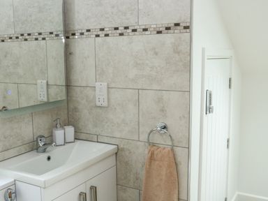 A bathroom sink with a mirror soap dispenser and towel hanging on a ring at Sawtons Cottage 2 in Dawlish