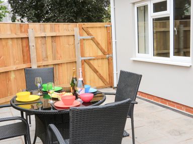 An outdoor patio with a round glass table set with colorful bowls plates and wine glasses surrounded by black wicker chairs at Sawtons Cottage 2 in Dawlish
