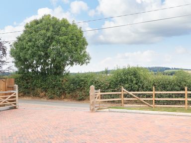 A paved driveway with wooden gates and a wooden fence with bushes and a large tree in the background at Sawtons Cottage 2 in Dawlish