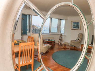A living room with wooden chairs a dining table two armchairs a round coffee table and a large window overlooking the sea at Port View in Falmouth