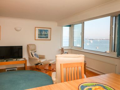 A living room with armchairs television and large windows overlooking a sea view at Port View in Falmouth