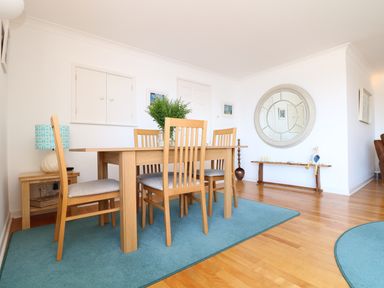A dining area with wooden table and chairs on a blue rug with a round mirror on the wall at Port View in Falmouth