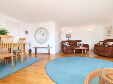 A living room with brown sofas, blue rugs, wooden dining table and chairs and a round wall mirror at Port View in Falmouth