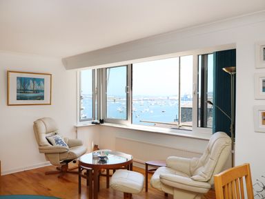 A sitting area with two armchairs and a round glass coffee table by a large window overlooking a harbor with boats at Port View in Falmouth