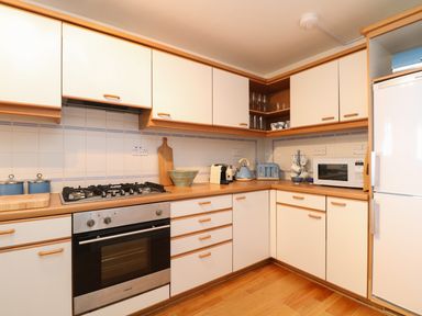 A kitchen with white cabinets wooden handles a gas stove an oven a microwave a refrigerator and small appliances at Port View in Falmouth