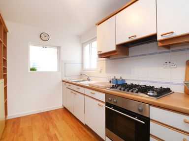 A kitchen with wooden cabinets a gas stove oven a sink and a clock on the wall at Port View in Falmouth