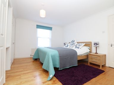 A bedroom with a bed covered in teal and gray bedding a wooden nightstand with a lamp and a window with a teal blind at Port View in Falmouth